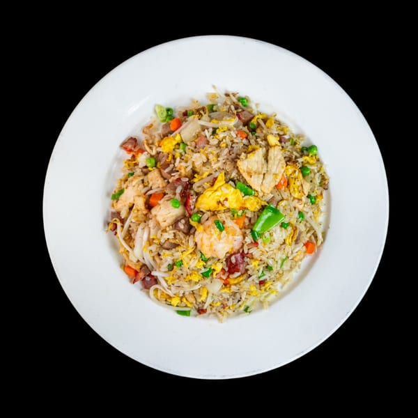 A white plate holds a colorful mix of fried rice with chicken, shrimp, pork, and vegetables.