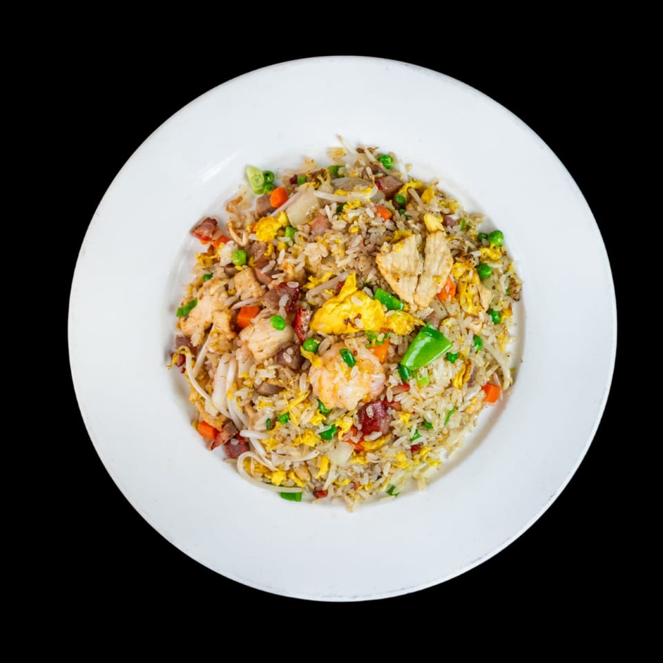 A white plate holds a colorful mix of fried rice with chicken, shrimp, pork, and vegetables.