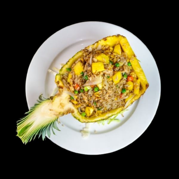 Pineapple fried rice, with peas, carrots, and pineapple chunks, served in a pineapple half.