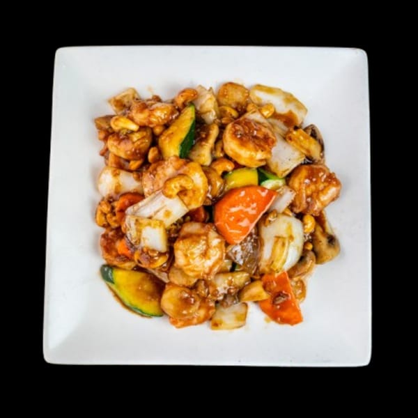 Cashew shrimp stir-fry with zucchini, bell peppers, and onions on a white square plate.